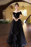 Woman in a black evening gown standing in an elegant indoor setting.