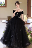 Woman in a black off-shoulder gown with pearl details sitting at a table.