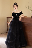 Woman in a black evening gown with a beaded top, standing indoors.