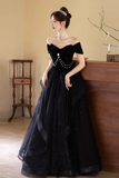 Woman in a black evening gown with a pearl necklace in an indoor setting.