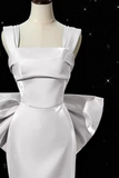 White evening gown with a large bow on a mannequin against a black background