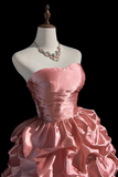 Pink strapless gown on a mannequin with a necklace against a black background
