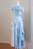 A light blue off-the-shoulder dress with tiered ruffle layers, displayed on a white mannequin in an indoor setting with a beige wall and wooden floor.