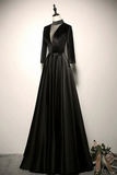 A floor-length black formal gown displayed on a mannequin against a plain light wall. The dress has a high neckline, long sleeves, a structured waist, and a full skirt.