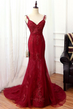 A deep red lace and tulle mermaid-style evening gown displayed on a mannequin in an indoor room with white curtains, wood flooring, and a dark armchair at the side.