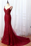 A deep red lace mermaid-style evening gown displayed on a mannequin in front of sheer white curtains and a wooden floor.