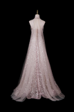 A sleeveless A-line evening gown displayed on a dress form against a solid black background. The dress features a sheer mesh overlay in a pale blush pink color heavily embellished with vertical columns of shimmering rose gold sequins.