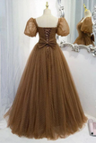 A brown tulle ball gown with a polka dot pattern, displayed on a mannequin. The dress features puff sleeves, a square neckline with lace-up front detailing, and a full, voluminous skirt.
