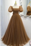 A brown tulle ball gown with a polka dot pattern, displayed on a mannequin. The dress features a square neckline, sheer puff sleeves, and a full, voluminous skirt.