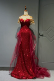 A formal red sequined gown displayed on a mannequin in an indoor room. The dress has a sweetheart neckline, sheer lace cap sleeves, a fitted bodice, and a long train with layered tulle draping over the sides.