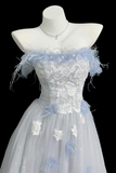 A strapless formal gown displayed on a white mannequin against a black background. The dress features a light blue and white floral lace bodice with feathered details, a white lace corset-style waist, and a voluminous tulle skirt with scattered white and light blue floral appliqués.