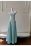 A light aqua blue maxi dress with thin spaghetti straps and a fitted silhouette, displayed on a white mannequin in an elegant room with a white bench and wood floors.