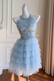 A light blue tulle dress with a beaded halter bodice and layered ruffle skirt, displayed on a white mannequin in an indoor room with cream paneled walls and curtains.
