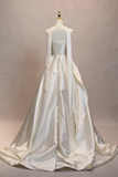 A white satin wedding gown displayed on a mannequin from the back, featuring a structured corset-style back with lace-up detailing and long draped ribbon tails on a plain beige studio background.