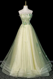 A pale yellow-green strapless tulle ball gown displayed on a mannequin against a black background. The dress features a fitted bodice with floral applique in matching green and white, a sheer embroidered bodice, and a voluminous layered tulle skirt.