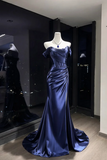 A floor-length off-the-shoulder evening gown in deep navy blue satin, displayed on a mannequin with a matching necklace inside a boutique showroom.