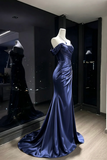 A floor-length off-the-shoulder evening gown in deep navy blue satin, displayed on a white mannequin in a boutique showroom. The dress features a fitted bodice, ruched waist, and a flared mermaid skirt with a long train.