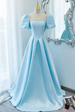 A light blue A-line ball gown with puff sleeves and scattered pearl embellishments, displayed on a mannequin in a bright room with a large ornate mirror.