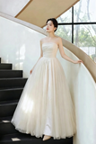 A woman wearing a strapless ivory tulle ball gown stands on a modern spiral staircase, holding the white handrail.