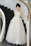 A woman wearing a strapless white ball gown with a structured satin bodice and a voluminous tulle skirt, standing on a modern black staircase with white railings.