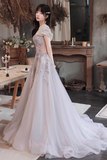 A woman wearing a voluminous off-white wedding gown with floral lace appliques and a short puff sleeve, standing in a rustic indoor setting with a wooden table and mirror in the background.