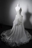 A white strapless wedding gown displayed on a white mannequin, featuring a structured corset bodice, a large draped overskirt, and a long flowing train against a dark studio background.