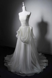 A strapless white wedding gown displayed on a white mannequin against a dark gray studio background. The dress features a ruched bodice, a draped waist detail, and a full flowing skirt with a train.
