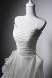 A strapless white wedding gown with a ruched bodice and layered tulle skirt, displayed on a white mannequin against a dark gray studio background.